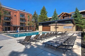 A poolside area with lounge chairs, a pool, and a building with multiple floors and balconies. - Park Station Condo in Old Town Park City | Walk to Town Lift, No Stairs + Heated Pool! (Park City)