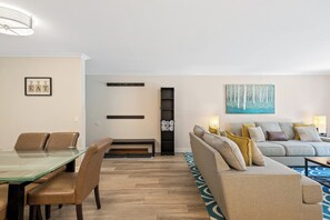 Uma sala de estar moderna com uma mesa de jantar de vidro, cadeiras de couro, um sofá e um quadro na parede.