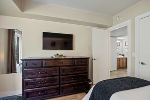 A bedroom with a large wooden dresser, a flat-screen TV mounted above it, and a door leading to a bathroom. - Park Station Condo in Old Town Park City | Walk to Town Lift, No Stairs + Heated Pool! (Park City)