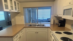 A kitchen with white cabinets, a double sink, a stove, and a view to a balcony with chairs. - New Port Richey Retreat- Sleeps 4 (New Port Richey)