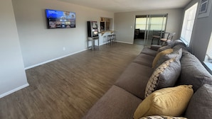 A spacious living area with a large flat-screen TV mounted on the wall, a kitchen area with a bar counter, and a sliding glass door leading to a balcony. - New Port Richey Retreat- Sleeps 4 (New Port Richey)