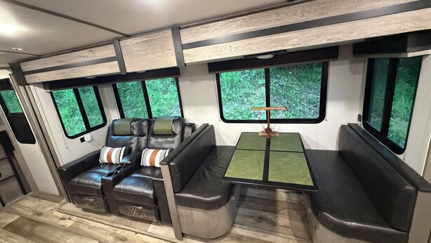 Interno di un treno con sedili, un tavolo e finestrini che danno su una vista verdeggiante.
