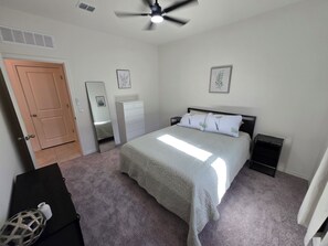 Ein Schlafzimmer mit Bett, Schminktisch, Spiegel, Deckenventilator und einer Tür.