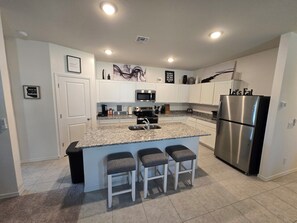 A modern kitchen with white cabinets, a stainless steel refrigerator, granite countertops, and three bar stools.