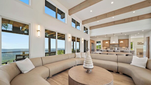 A spacious living area with a large L-shaped sectional sofa, a round coffee table, and a view of the ocean. - High View: Brand-New 5,100 Sq Ft Nordic-Inspired Mountain Estate with Four-State Views (Banner Elk)