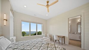 A bedroom with a large bed, a desk, a chair, a ceiling fan, and a view of the outdoors. - High View: Brand-New 5,100 Sq Ft Nordic-Inspired Mountain Estate with Four-State Views (Banner Elk)