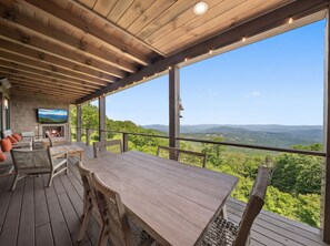 An outdoor deck with a wooden table and chairs, a fireplace, and a view of the mountains. - High View: Brand-New 5,100 Sq Ft Nordic-Inspired Mountain Estate with Four-State Views (Banner Elk)