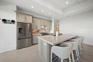 A modern kitchen with stainless steel appliances, a marble countertop, and bar stools. - High View: Brand-New 5,100 Sq Ft Nordic-Inspired Mountain Estate with Four-State Views (Banner Elk)