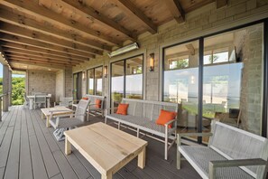 An outdoor covered patio with wooden tables and benches, large windows, and a stone wall. - High View: Brand-New 5,100 Sq Ft Nordic-Inspired Mountain Estate with Four-State Views (Banner Elk)