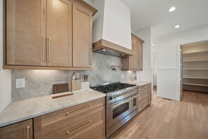 A modern kitchen with wooden cabinets, a stainless steel stove, and a marble countertop. - High View: Brand-New 5,100 Sq Ft Nordic-Inspired Mountain Estate with Four-State Views (Banner Elk)