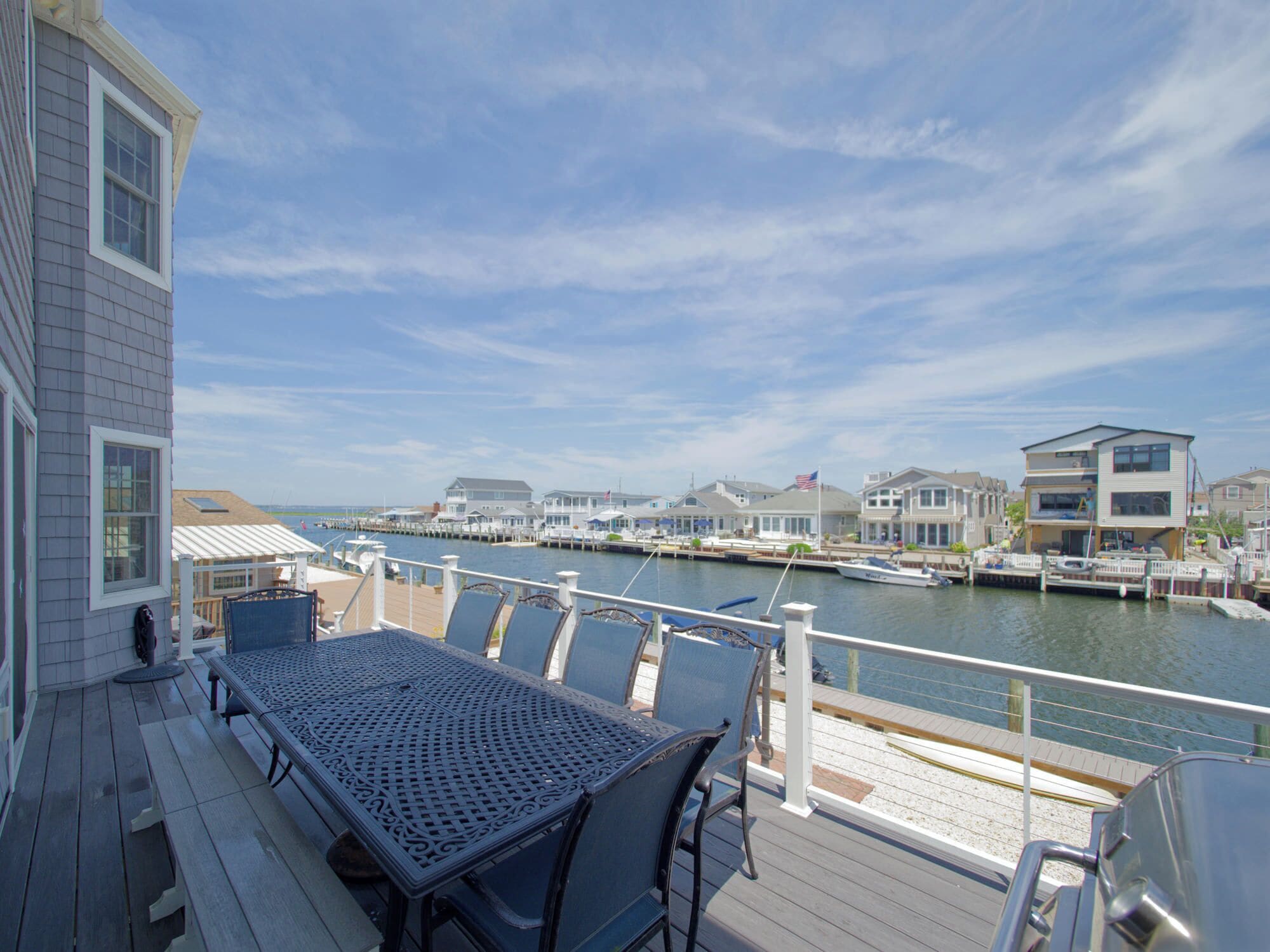 A deck with a table and chairs overlooking a marina with boats and houses.