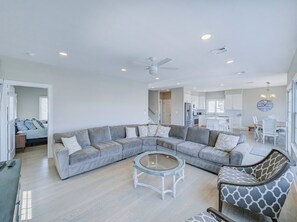 Ein geräumiges Wohnzimmer mit einem großen, winkelförmigen Ecksofa, einem runden Couchtisch und einem Ohrensessel mit Giraffenmuster.