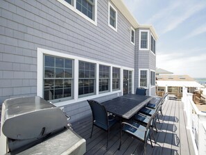 Eine Terrasse mit Grill, Esstisch und Stühlen mit Blick auf ein Gewässer.