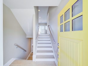 Eine Treppe führt zu einer gelben Tür mit einem Fenster, einer Handläufe und einem Blick ins Innere.