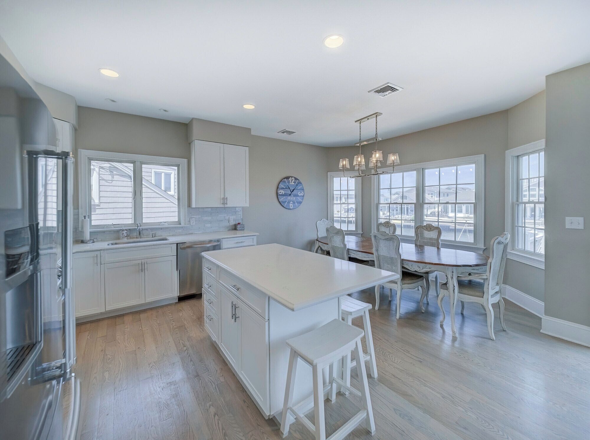 A kitchen with white cabinetry, a central island, and a dining area with white chairs.
