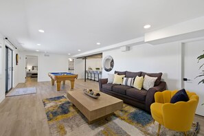 Ein modernes Wohnzimmer mit Billardtisch, einer Couch, einem gelben Sessel und einem Couchtisch.
