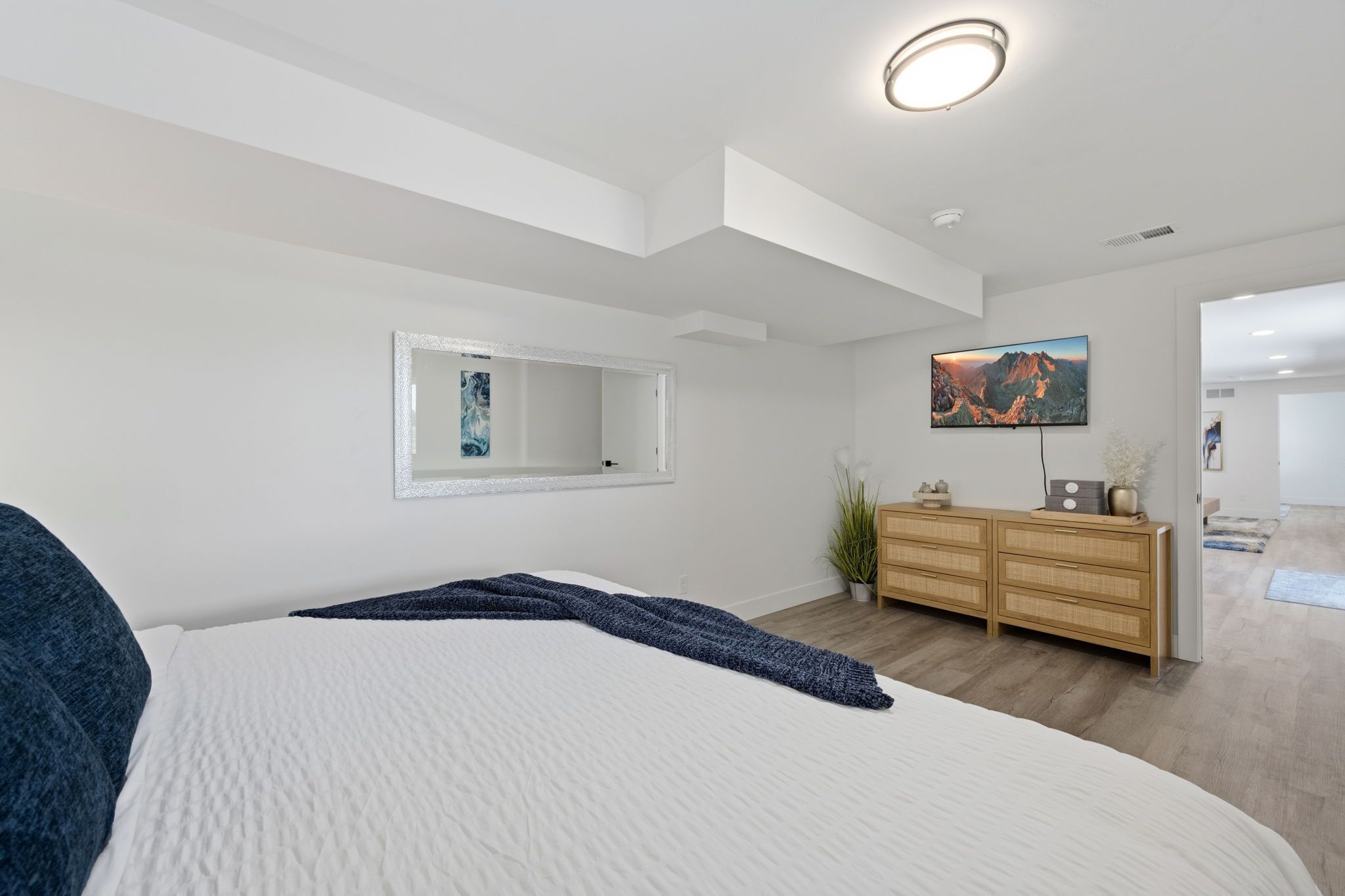 Une chambre à coucher moderne avec un grand lit, une commode, un miroir et un tableau accroché au mur.
