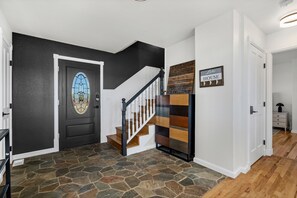 Eine Treppe mit hölzernem Geländer und weißen Spindeln, eine schwarze Tür mit einem Glasfenster im Buntglasstil und eine Wand mit einem Schild ‚Like House‘.