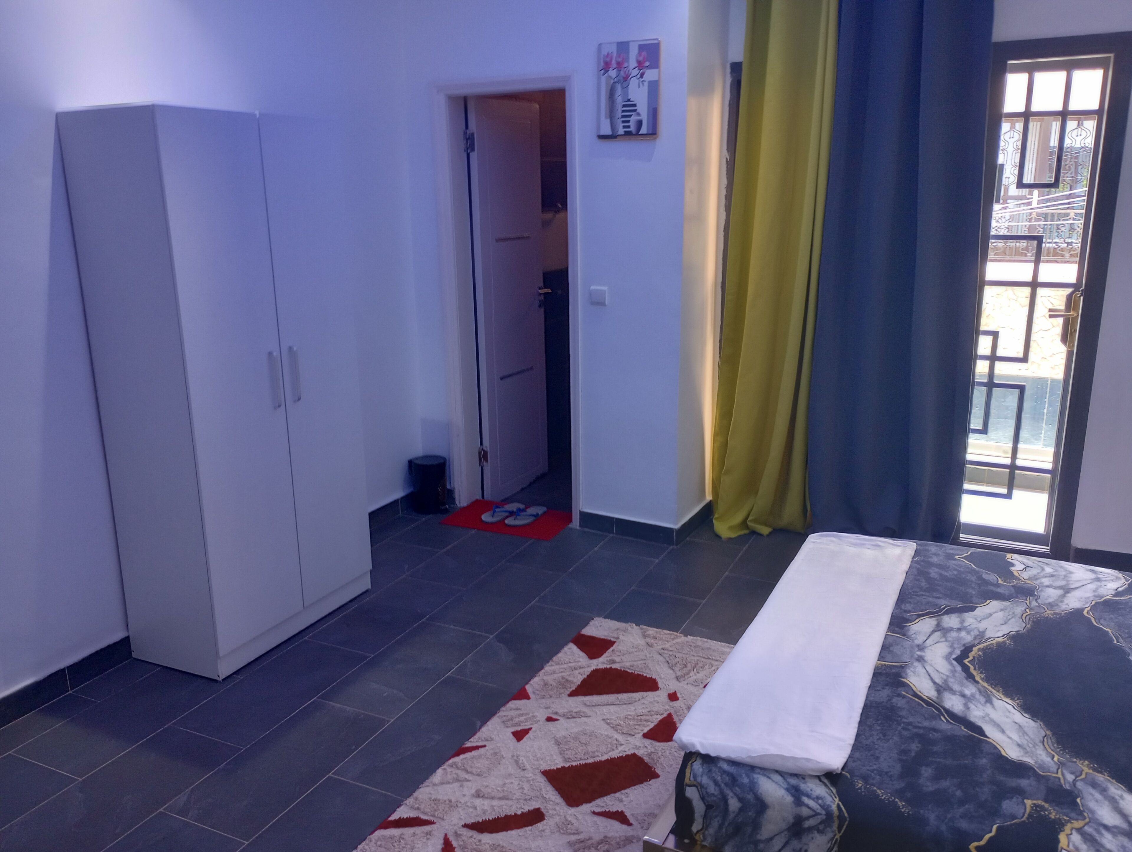 A bedroom with a bed, a wardrobe, a door leading to a bathroom, and a window with curtains.