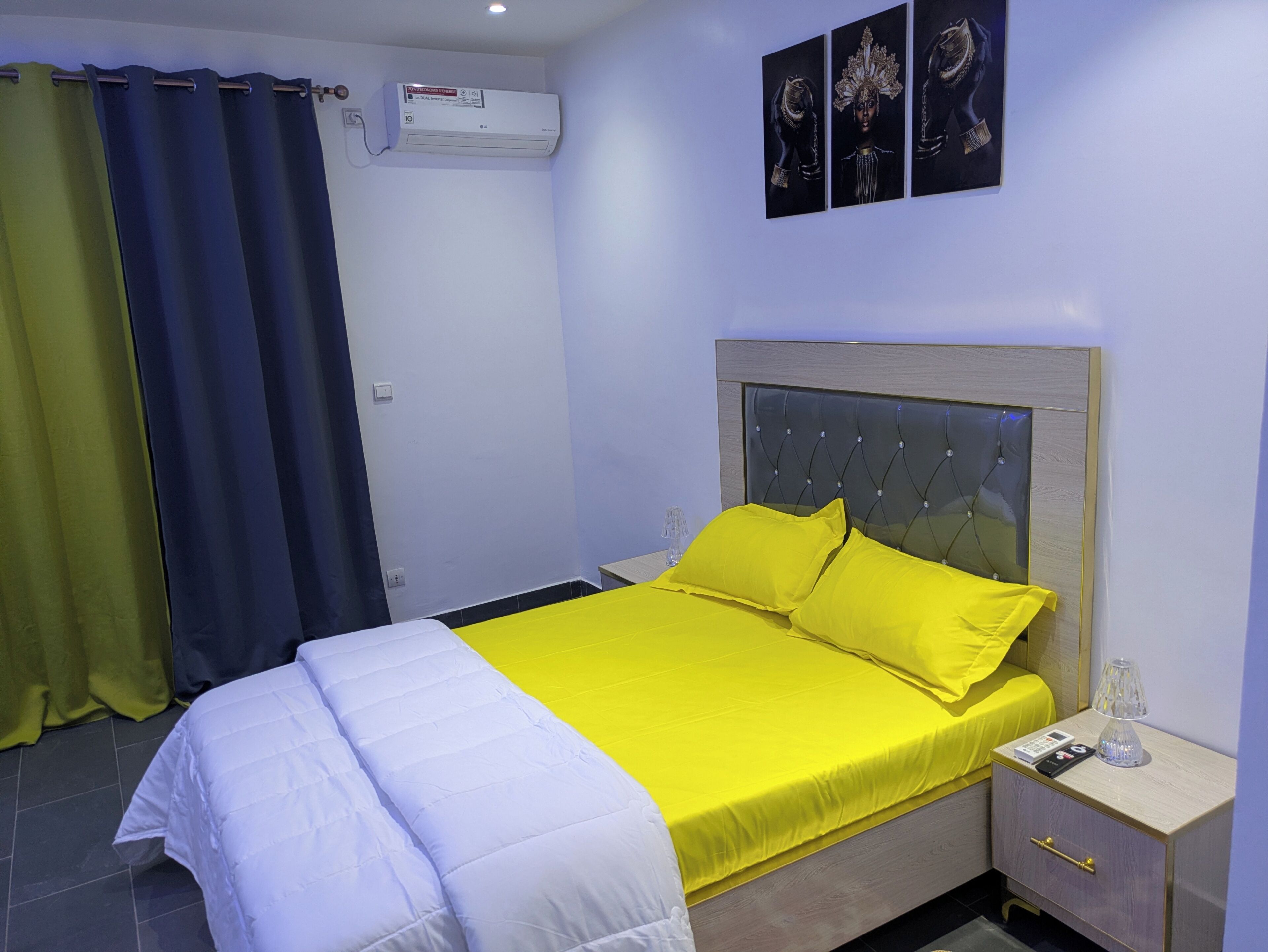 A hotel room with a bed, a nightstand, a lamp, and a wall-mounted air conditioner.