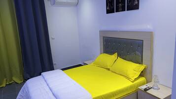 A hotel room with a bed, a nightstand, a lamp, and a wall-mounted air conditioner.