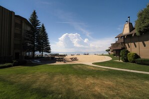 A beach area with picnic tables and umbrellas, a building with a chimney, and a large tree. - Rare Beach Front Condo in South Lake Tahoe (South Lake Tahoe)