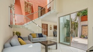 A modern living room with a staircase, a sofa, a coffee table, and a glass door leading to an outdoor area with plants. - Casa Mamino Pool Palapa & Pet Friendly (Cuernavaca)