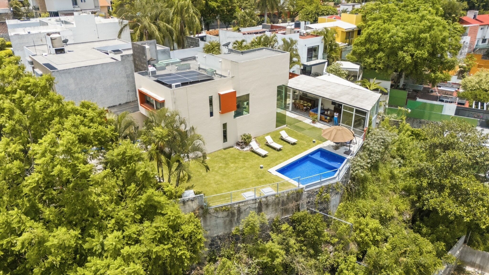 Un edificio moderno con piscina en la azotea, rodeado de exuberante vegetación.