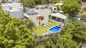 Un edificio moderno con piscina en la azotea, rodeado de exuberante vegetación.