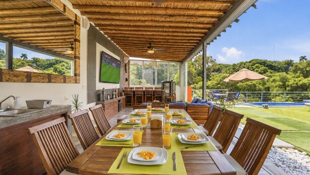 A covered dining area with a table set for breakfast, a TV, and a pool in the background. - Casa Mamino Pool Palapa & Pet Friendly (Cuernavaca)