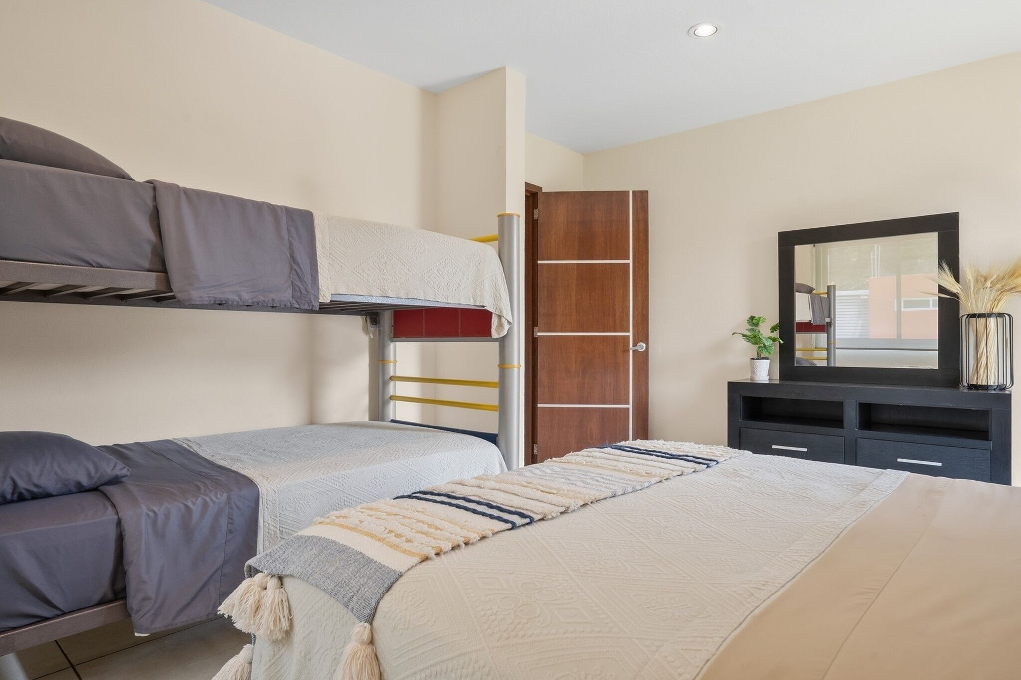 A bedroom with bunk beds, a bedside table, a mirror, and a dresser.