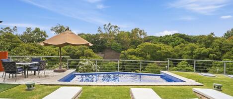 A pool area with lounge chairs, a table, and an umbrella.