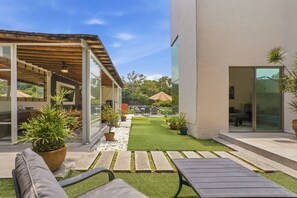 Un patio moderno al aire libre con zona de estar, césped pequeño y plantas en macetas.