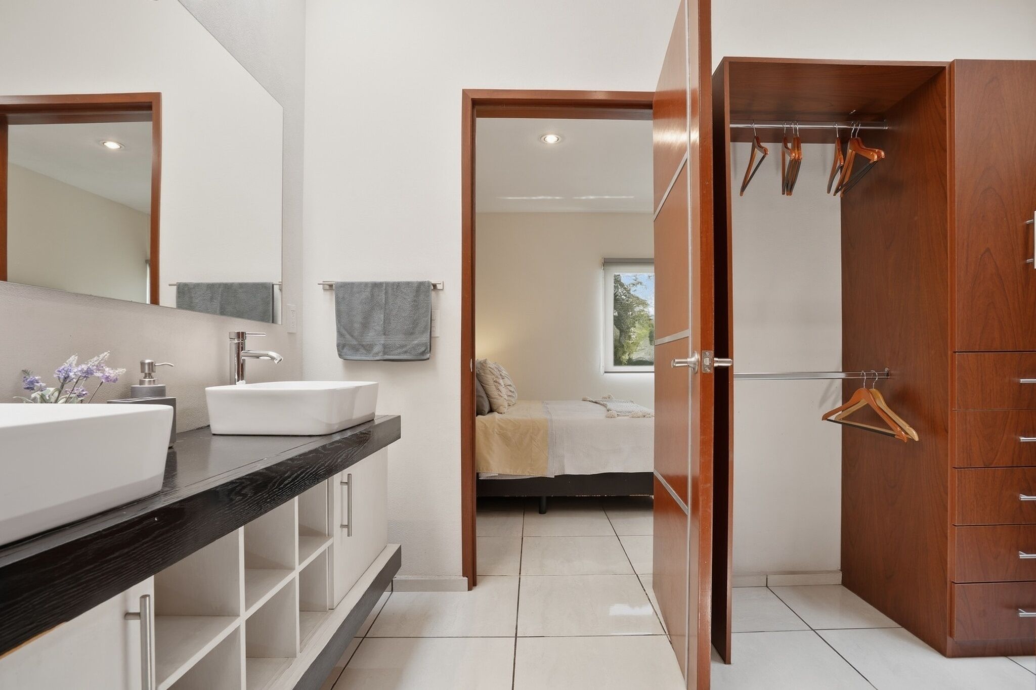 A modern bathroom with a large mirror, a white sink, and a wooden wardrobe.