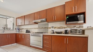 A modern kitchen with wooden cabinets, a built-in microwave, a stove, and a toaster. - Casa Mamino Pool Palapa & Pet Friendly (Cuernavaca)
