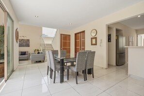 Una cocina moderna con refrigerador integrado, una zona de comedor con mesa de vidrio y sillas grises, y una escalera que lleva a un nivel superior.