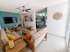A modern living room with a sofa, coffee table, and TV. There is a kitchen in the background with cabinets and a dining area. - Cozy 3BR house with AC•Parking•Patio•Centric Location
Casa Jeyri (Cataño)