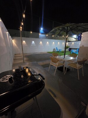 Ein Terrassenbereich im Freien mit Grill, Stühlen und Lichterketten.