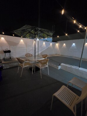 Ein Terrassenbereich im Freien mit Tisch und Stühlen, Lichterketten und einer überdachten Sitzgelegenheit.