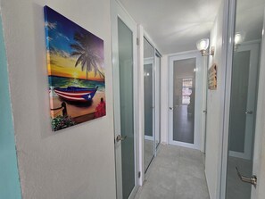 En hall med en målning av en båt på en strand, dörrar som leder till andra rum och en lampa på väggen.