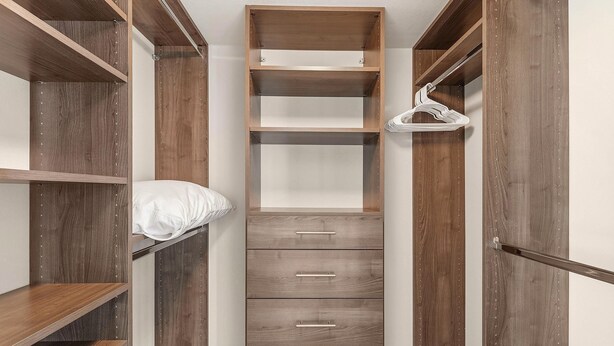 Un armario vestidor con estantes de madera, cajones y barra para colgar.