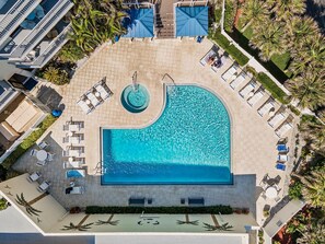 Ein großer Pool, umgeben von Liegestühlen und Sonnenliegen, mit einem runden Whirlpool in der Mitte.