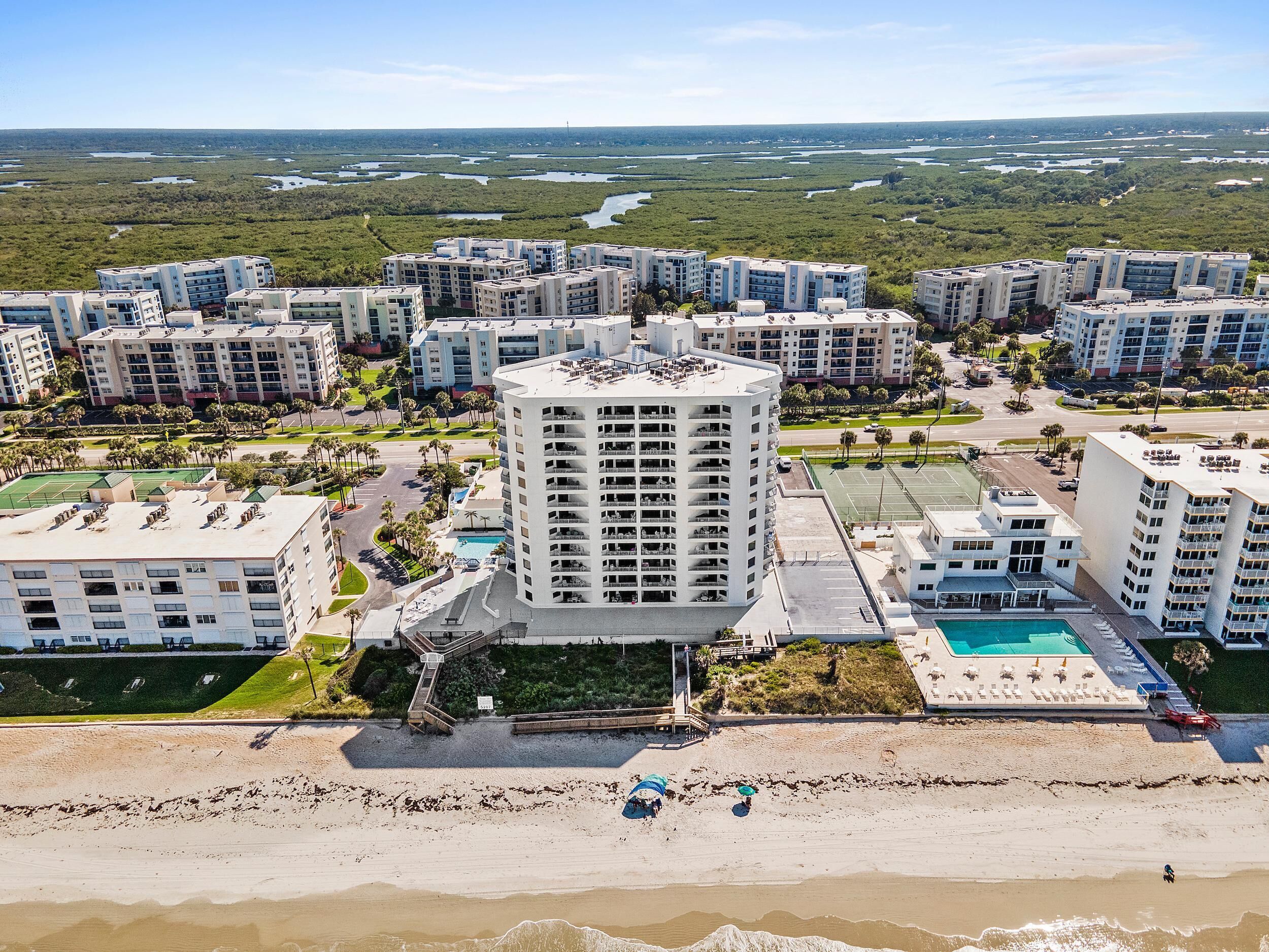 A high-rise hotel with multiple floors, a rooftop pool, and a beach area with umbrellas.