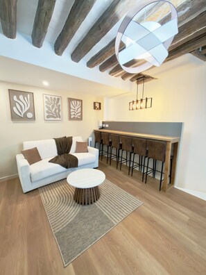 Uma sala de estar moderna com um sofá branco, uma mesa de centro redonda e um espaço bar com banquetas.