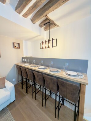 Uma área de jantar moderna com uma mesa comprida, várias cadeiras e um lustre pendurado.