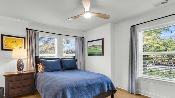 Una camera da letto con un letto, un comodino, una lampada, un ventilatore a soffitto e una finestra con tende.