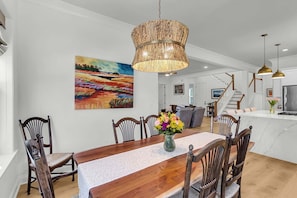 Ein Essbereich mit Holztisch, Stühlen, einer geflochtenen Pendelleuchte und einem farbenfrohen Bild an der Wand.