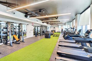 Ein Fitnessstudio mit Laufbändern, Krafttrainingsgeräten und einem Teppichbereich in Grün.