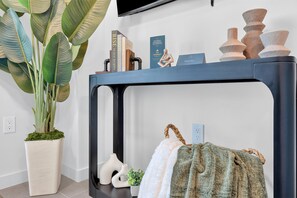 Ein Zimmer mit einem schwarzen Konsolentisch, einer Topfpflanze, einem an der Wand montierten Fernseher und einigen Dekorationsgegenständen.