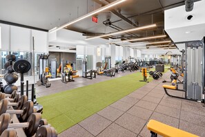 Ein Fitnessstudio mit unterschiedlichen Trainingsgeräten, einem grünen Rasenbereich und Blick auf die Stadt durch große Fenster.